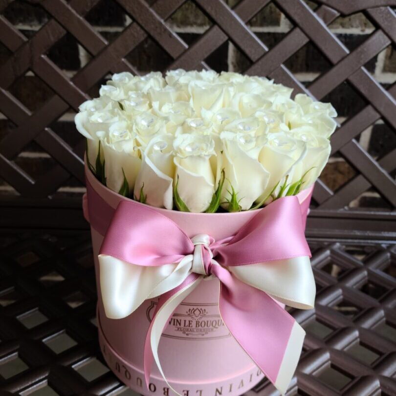 A pink hat box with white roses in it.